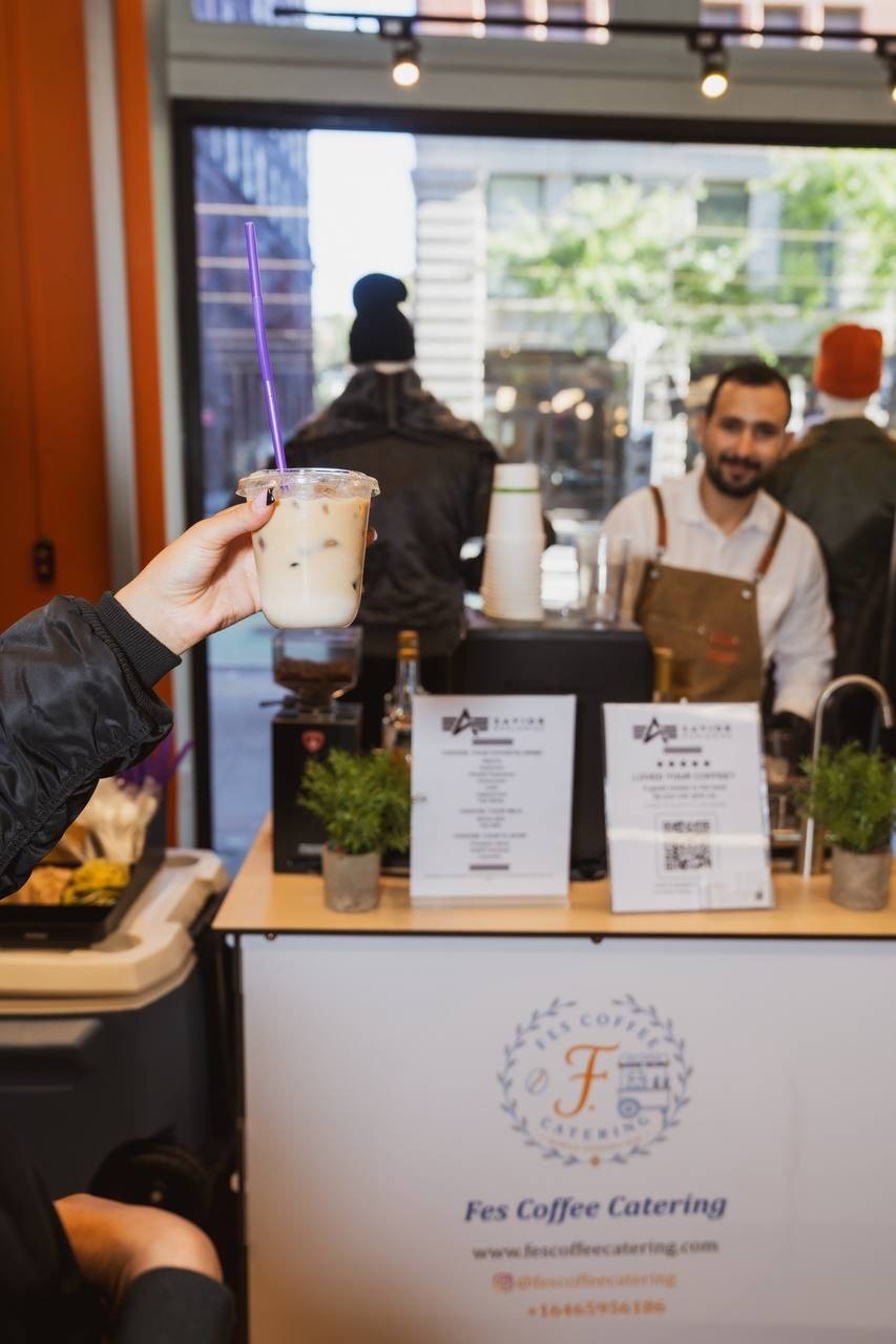 Barista smiling behind the Fes Coffee cart while a guest holds up an iced drink