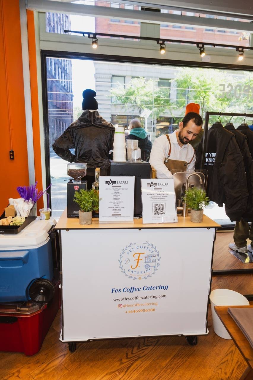Front view of the Fes Coffee cart with menu signs and a barista behind it at an in-store event