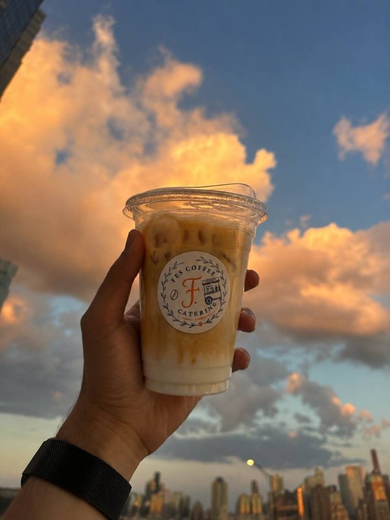Iced latte in a Fes Coffee cup against a sunset sky