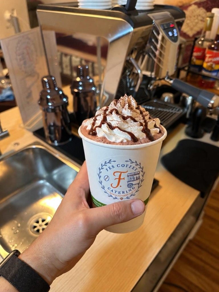 Hot chocolate with whipped cream and chocolate drizzle in a Fes Coffee cup